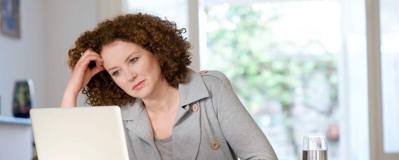 pensive curly haired woman working on her laptop